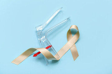 Beige ribbon with gynecological tool on blue background. Uterine cancer awareness concept