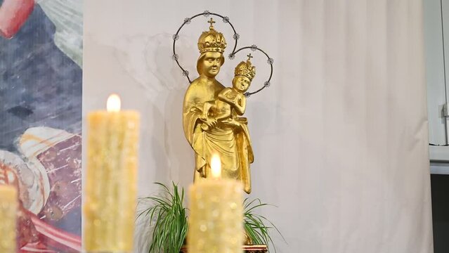 Lighted candles in the church. A statue of the Virgin Mary and Jesus Christ in the background. Decorated altar for Christmas.