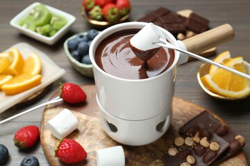Dipping sweet marshmallow in fondue pot with melted chocolate at wooden table