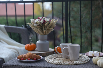 Snacking outdoors. Rattan table with cups of drink, croissant and autumn decor on terrace