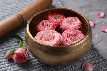Tibetan singing bowl with water, beautiful roses and mallet on grey textured table, closeup