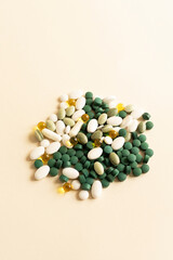 Assorted Pile of Colorful Pills, Green White Yellow, Beige Tablets, Capsules, Medical Supplement on Beige Background. Pharmaceutical concept. Copy Space For Text. Vertical Plane