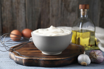Tasty mayonnaise in bowl and ingredients on light grey wooden table, closeup