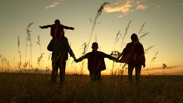 Silhouette family, Dad mom daughter son go hand in hand outdoors in autumn. Parental care for children, Big family, group of people, nature. Active family with children walks in grass field in summer.