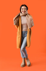 Beautiful young Asian woman in warm scarf on orange background