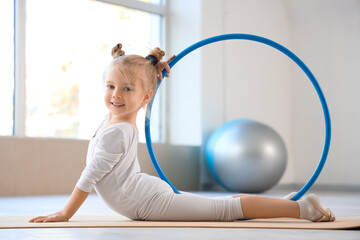 Cute little girl doing gymnastics with hula hoop on mat in gym