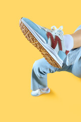 Female legs in stylish sneakers on yellow background, closeup