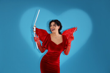 Young African-American woman dressed as Cupid with bow on blue background. Valentine's Day...