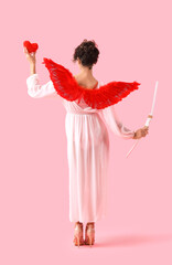 Young woman dressed as Cupid with heart and bow on pink background, back view. Valentine's Day...