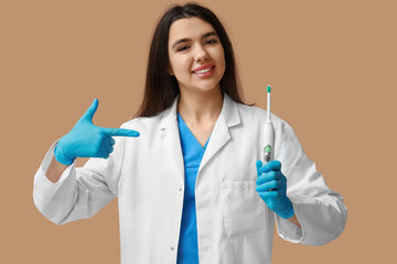 Female dentist pointing at electric toothbrush on brown background. World Dentist Day