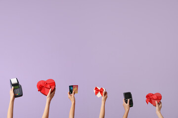 Women with payment terminals, credit cards and gifts on lilac background. Valentine's Day celebration