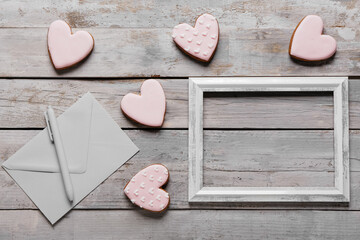 Tasty heart shaped cookies with photo frame, envelope and pen on grey wooden background. Valentine's Day celebration