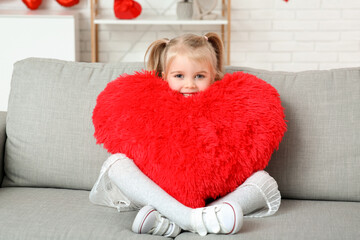 Cute little girl with heart shaped pillow sitting in room. Valentines Day celebration
