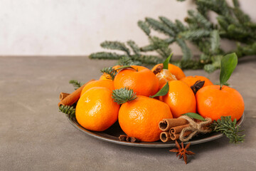 Plate of sweet mandarins with cinnamon, star anise and fir branches on grey table