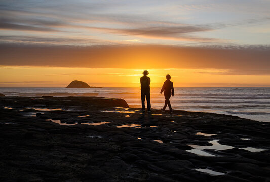 Couple enjoy the sunset at Muriwai beach. Oaia Island in the distance. Auckland.