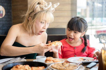 Happy mother and daughter Having Pizza in a Restaurant. Happy family craving for fast food meal