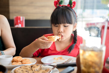Happy asian little girl eat pizza on table at restaurant
