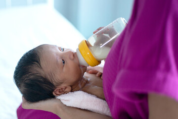 Happy little baby drinking milk from a bottle in mother's arms, mother feed her baby while sitting on bed