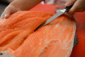 Fresh salmon fillet close-up on white cutting board table while filleting salmon belly by chef in cooking room - obrazy, fototapety, plakaty