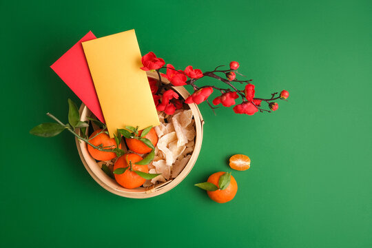 Tangerines, ginger jam, peach blossom branches and lucky money envelopes inside a bamboo steamer on a green background. Free space for design.