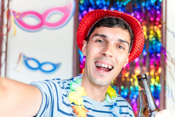 Young Brazilian man in carnival attire takes a cheerful selfie with his phone, smiling while enjoying a beer bottle