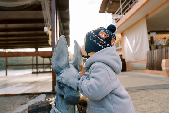 Little girl kisses the ear of a statue of a fabulous donkey loaded with barrels