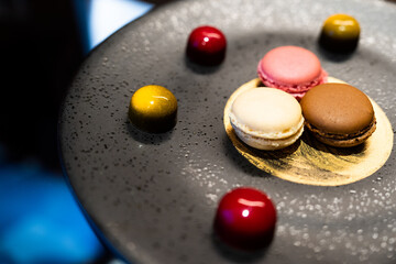 Pastel macarons France sweet dessert with dark chocolate red and gold color around strawberry, coffee and vanilla flavors on luxury black dish for afternoon tea or birthday snack in the cafe
