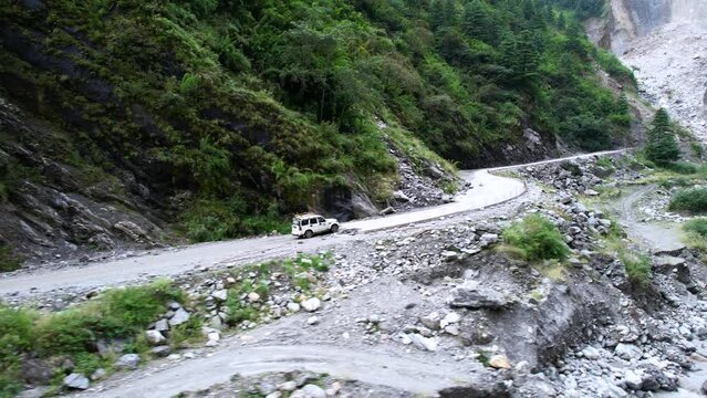 Aerial of 4x4 Safari Jeep transporting tourists off-road up a green rocky mountain landscape in Mustang Nepal
