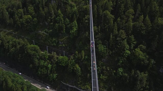 Aerial view of the world's longest pedestrian suspension bridge, connecting Ehrenberg Castle and Fort Claudia in Austria, over a busy road and surrounded by a forest of trees