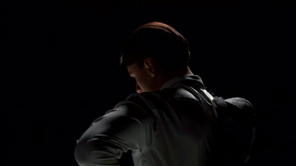 Rear view of attractive man putting on suit. Stock footage. Man takes jacket from chair and puts it on in front of mirror. Man wears costume on theatrical stage in single production