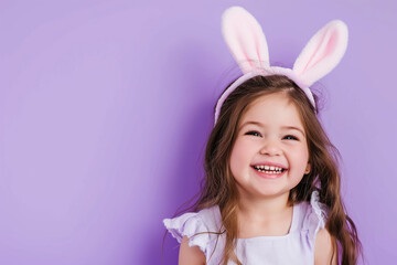 Obraz na płótnie Canvas little smiling girl with artificial bunny ears on her head on a purple background, Easter mood