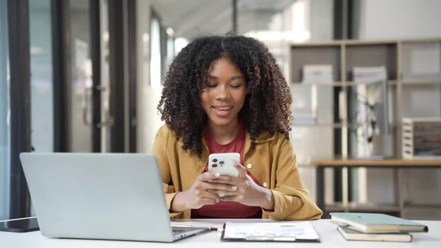 Beautiful African woman in business suit talking on mobile phone while working at table in office using modern smartphone to talk with client for consultation 4k 60p