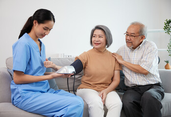 caregiver or nurse measure blood pressure to senior woman on sofa