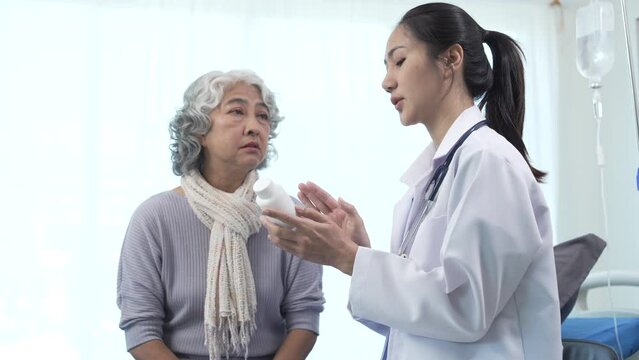 Elderly Asian woman lying in hospital bed looking unwell, with young Asian doctor take a history of illness Health check and encouragement.