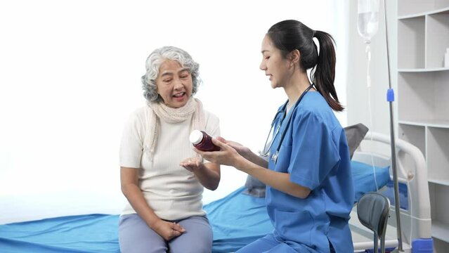 Asian care nurse checks senior Asian female patient on hospital bed. Attractive caregiver supports, gives advice and consults with elderly grandmother at clinic.4k 60p