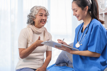 Health check concept, Elderly Asian woman with grey hair, sitting and talking to young Asian nurse by appointment, sitting on medical bed. - obrazy, fototapety, plakaty
