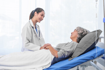 Obraz premium Elderly Asian woman lying in hospital bed looking unwell, with young Asian doctor take a history of illness Health check and encouragement.