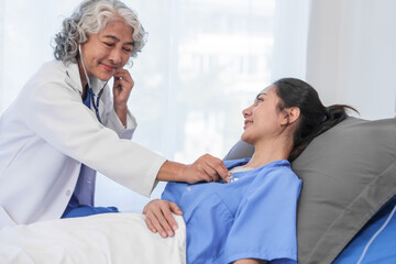 Fototapeta premium An elderly Asian doctor with a stethoscope is checking young Asian patient in hospital bed, take history of illness Health check and encouragement