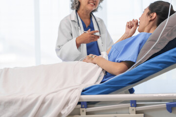 An elderly Asian doctor with a stethoscope is checking young Asian patient in hospital bed, take history of illness Health check and encouragement