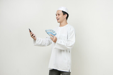 happy muslim man holding money rupiah banknotes and  mobile phone. People religious Islam lifestyle concept. celebration Ramadan and ied Mubarak. on isolated background.