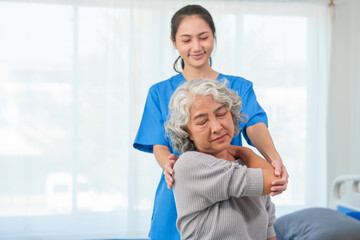 A young Asian nurse is assisting an elderly Asian woman with a grey hair during a physical therapy...