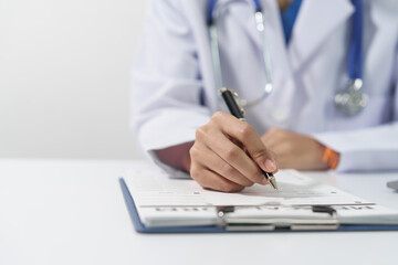 Medical doctor person hand is writing on a medical form on clipboard, on a white surface at medical desk.