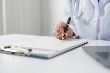 Medical doctor person hand is writing on a medical form on clipboard, on a white surface at medical desk.
