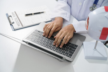 A doctor's hands are seen typing on a laptop keyboard with a stethoscope around the neck on white desk. - obrazy, fototapety, plakaty