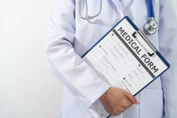 A doctor in a white coat is holding a clipboard with a medical form attached to it, with a...