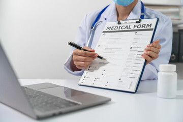 A doctor in a lab coat with a stethoscope is holding a medical form on a clipboard and pointing to it with a pen. - obrazy, fototapety, plakaty