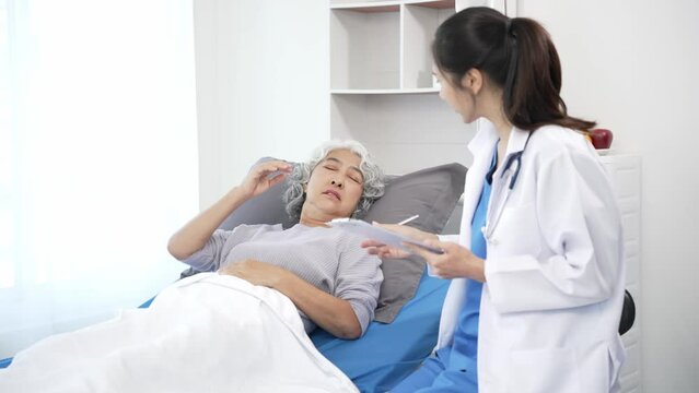 Asian care nurse checks senior Asian female patient on hospital bed. Attractive caregiver supports, gives advice and consults with elderly grandmother at clinic.4k 60p
