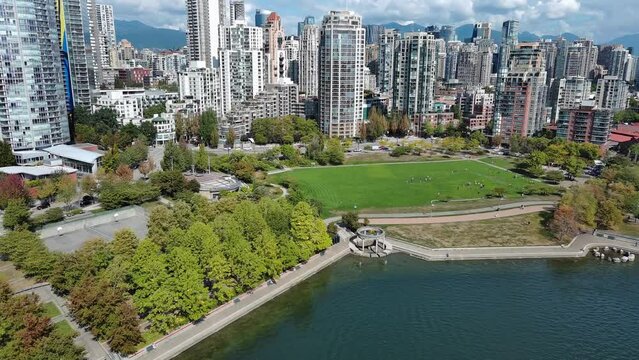 Drone shot of a park by downtown Vancouver buildings. David Lam park where kids are playing and seawall with people walking and running.