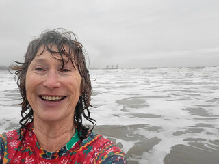 Mature woman wears a colourful Christmas themed rash vest while swimming in the sea over the Christmas holidays. She takes a selfie for a family photo messaging group.