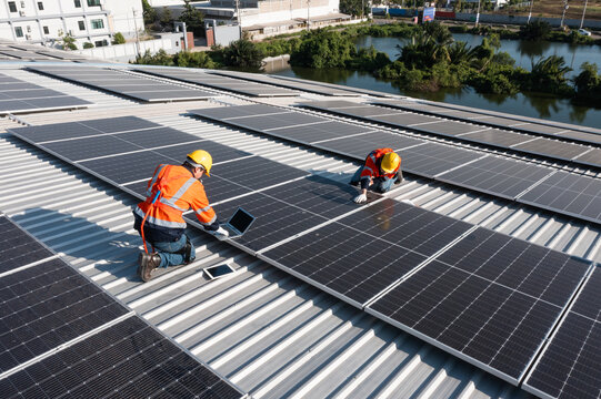 Two caucasian engineering technician is a professional trained in skills and techniques installing solar photovoltaic panels system on industrial factory roof, Engineering concepts to good environment